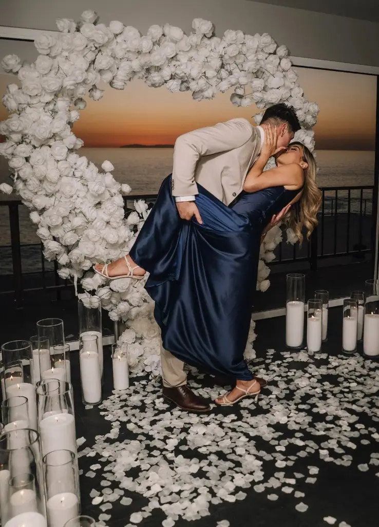 Couple kissing in a dip before a heart floral arch at sunset