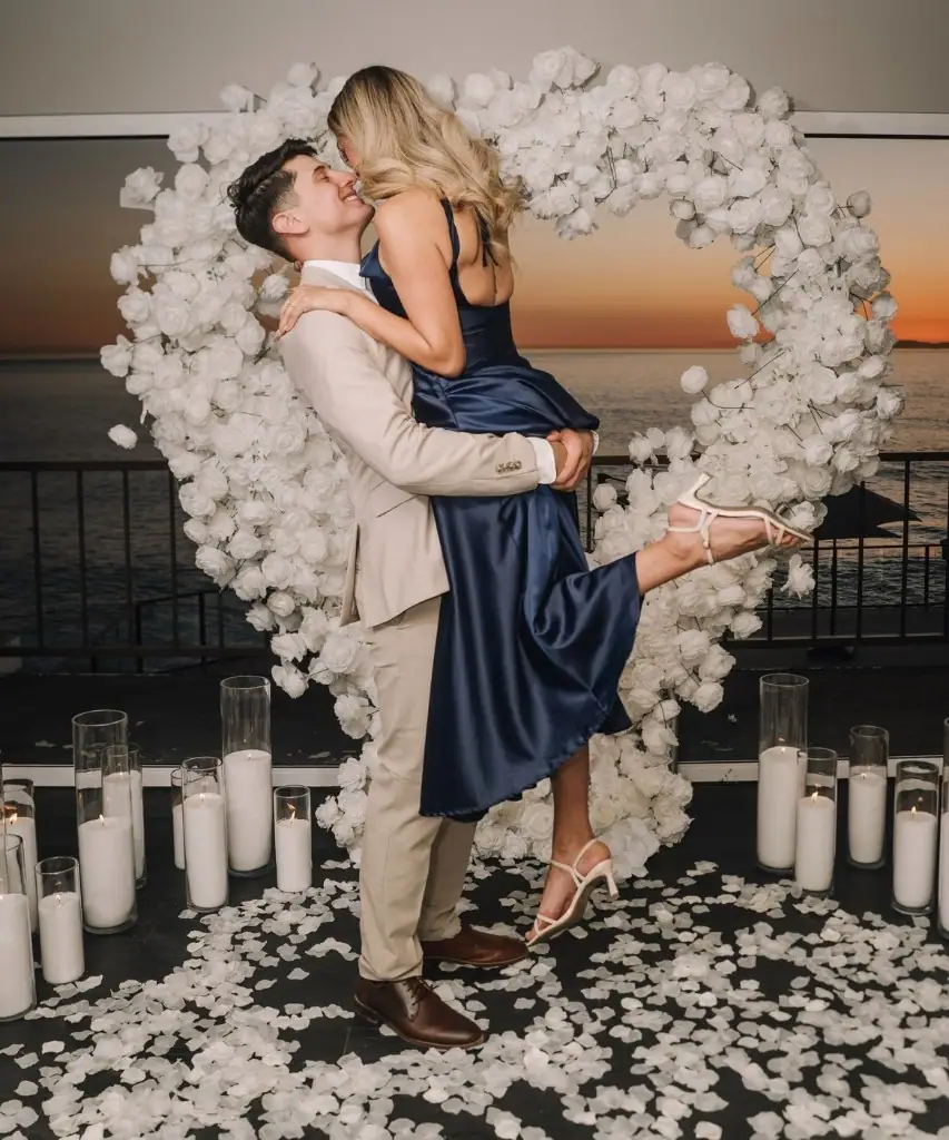Couple lifted in front of a white rose heart at ocean sunset
